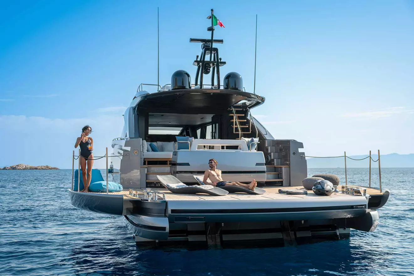 The stern of a Pershing GTX80 yacht at anchor, with two people relaxing on its expansive beach club platform