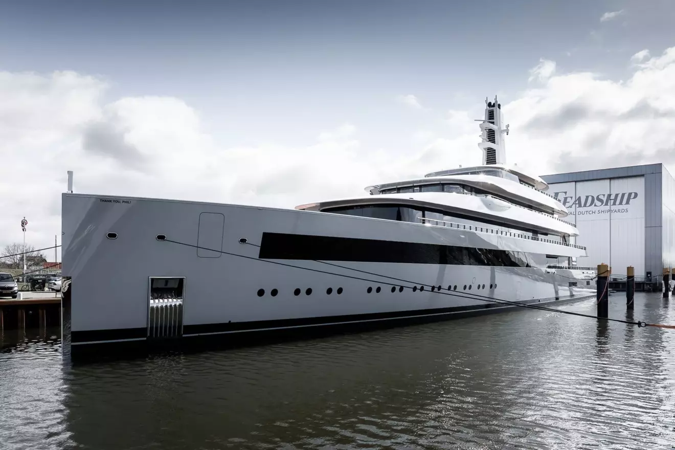 A wide shot of the luxury yacht Moonrise, a gray vessel built by Feadship, docked in calm water at a pier.