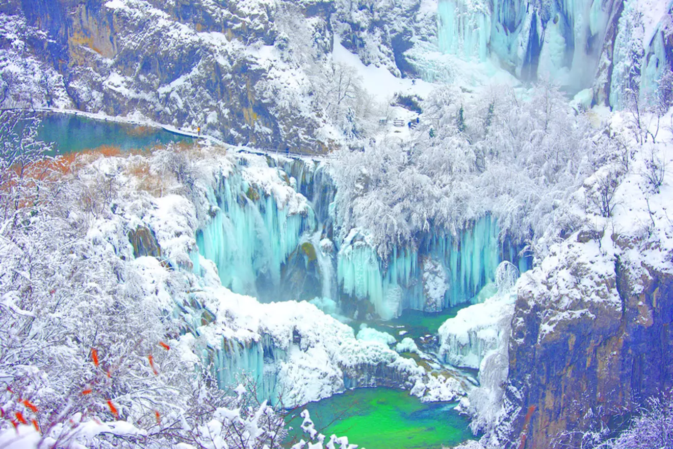 Frozen waterfalls and snow-covered trees at Plitvice Lakes National Park in winter.