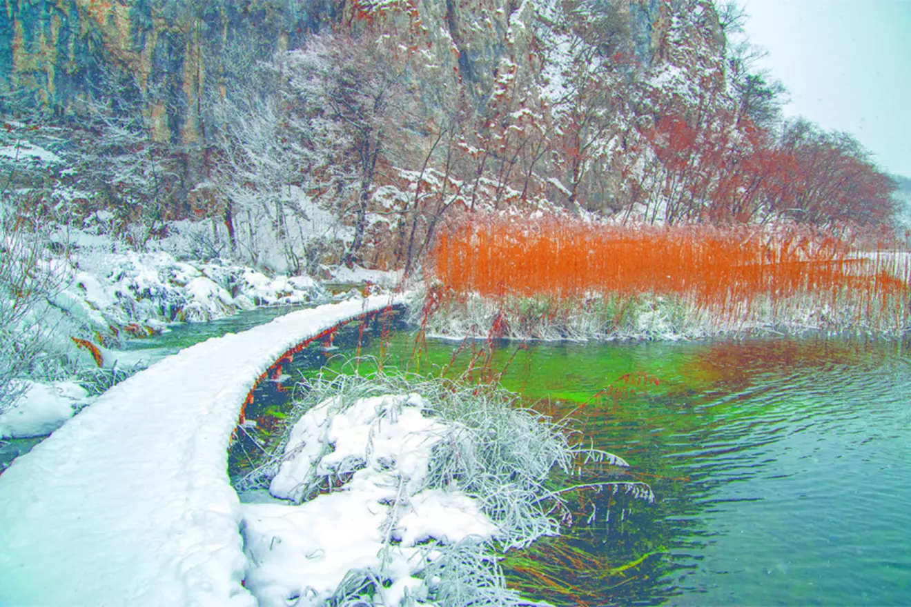 Snow-covered wooden walkway at Plitvice Lakes in winter.