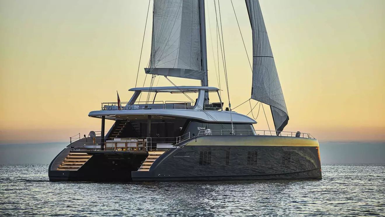 An 80 Sunreef sailing catamaran cruises at sunset.