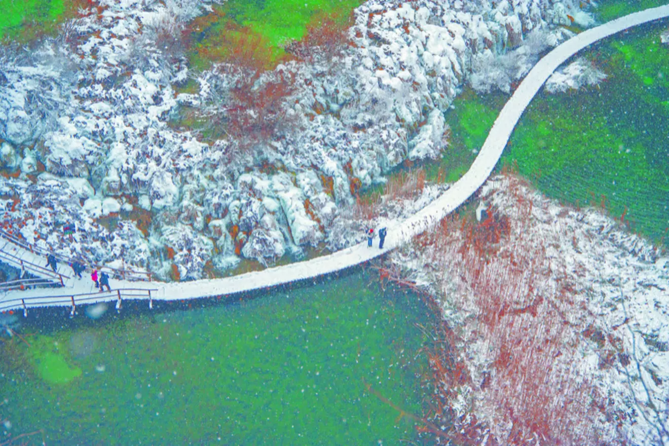 Visitors on a snow-covered trail at Plitvice Lakes National Park in winter.