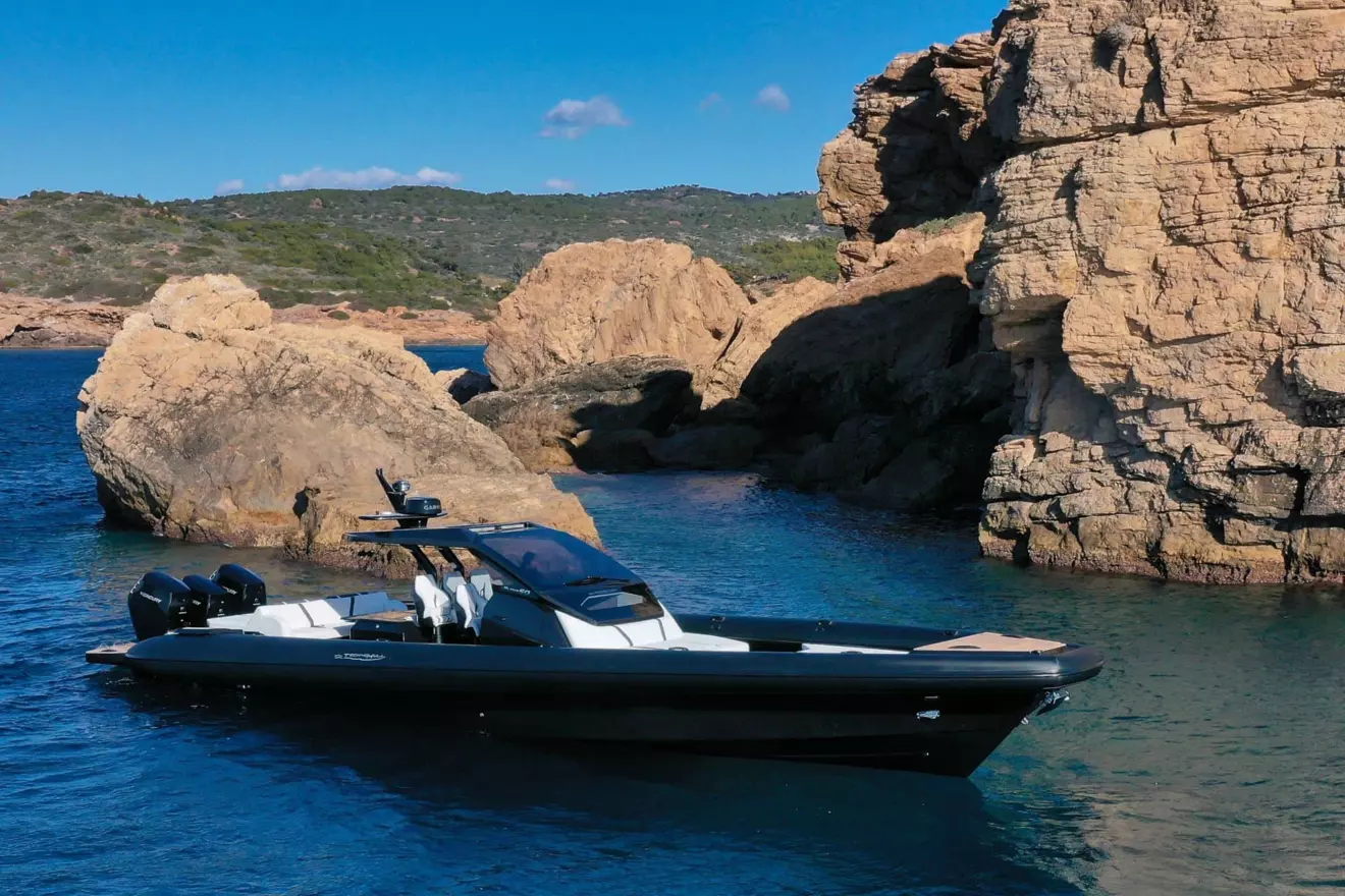 Technohull Alpha 50, a high-performance luxury RIB, with triple engines visible, positioned in a picturesque cove.
