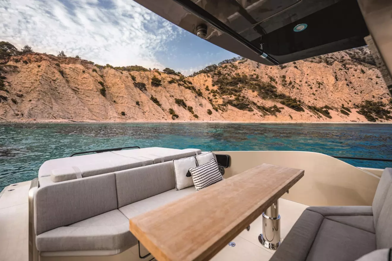 SACS Rebel 47 aft deck with seating and table, overlooking a rocky coastline and blue water.
