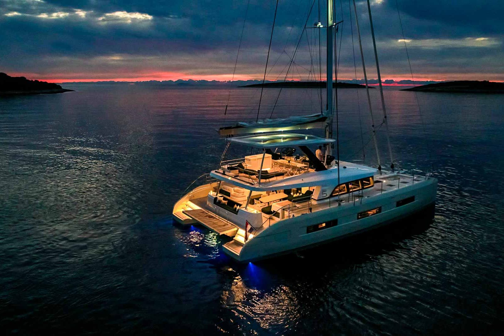 This is photo of a catamaran Lagoon Sixty5 named Amada Mia night lights, aerial view